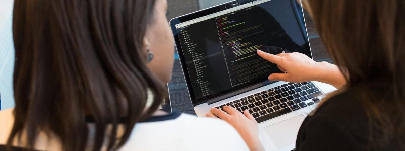 Two Women Looking at the Code at Laptop